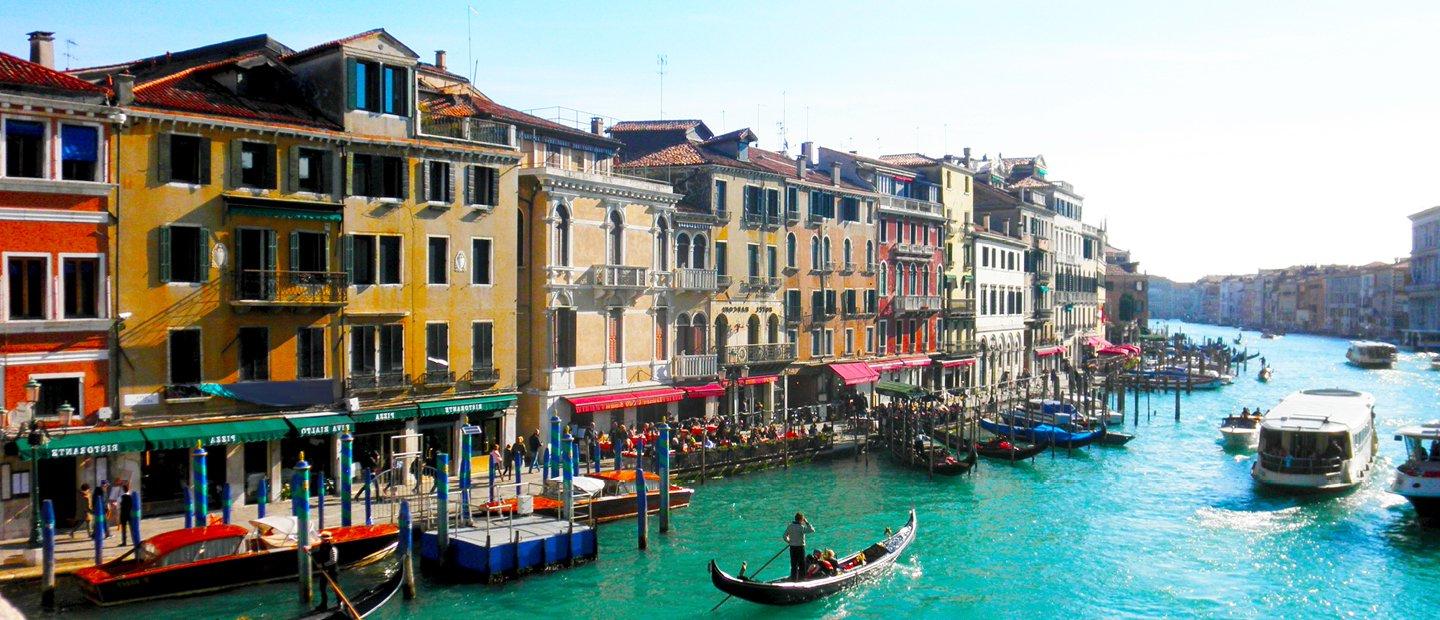 colorful buildings along either side of a river with boats in it, in Italy