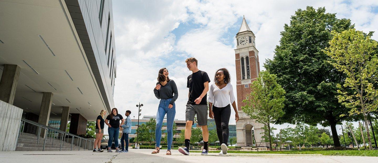 students walking on Oakland University's campus with a clock tower in the background