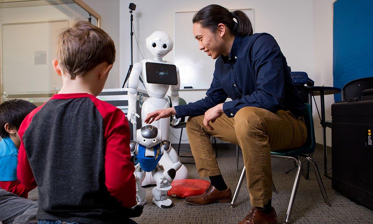 Man sitting on chair showing robots to two children
