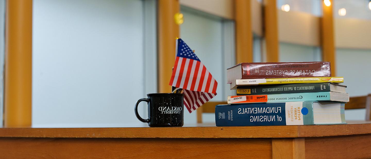Books stacked on a desk next to an American flag and coffee mug